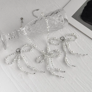 Elegant pearl bead necklace and bow tie earring set on a white textured background
