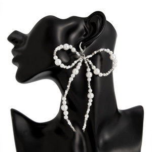 Detailed close-up of large white imitation pearl bow earrings on a black silhouette model