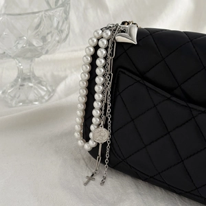 Detail einer gesteppten Ledertasche mit Perlen, Silbermünzen und Herz-Anhänger-Details