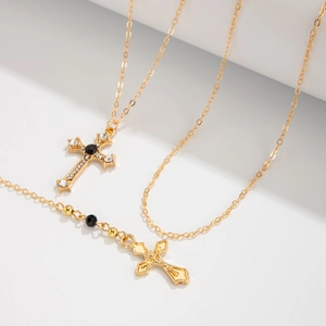 Détail de colliers croix en or avec strass noirs et blancs sur fond blanc épuré
