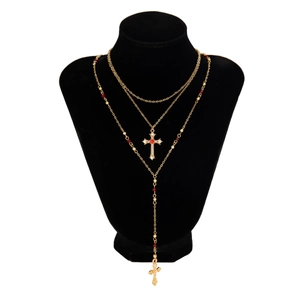Détail d'un collier en Y multicouche doré avec pendentifs croix en strass et perles rouges