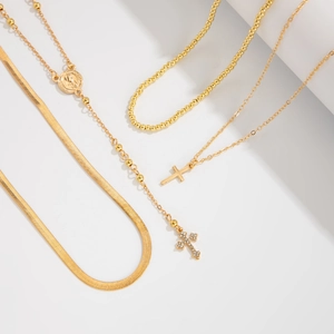 Détail de colliers dorés superposés avec croix sertie de diamants et pendentifs religieux