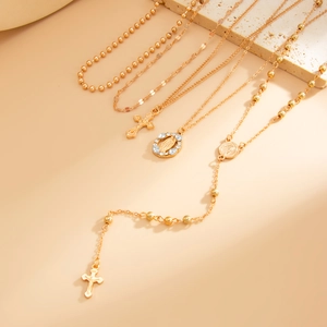 Détail de colliers dorés superposés avec pendentifs croix et médailles sur support en pierre
