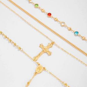Détail de colliers dorés superposés avec pierres colorées et pendentif de crucifix
