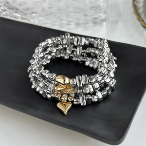 Detail eines silbernen Perlenarmbands mit goldenen Herzanhängern auf schwarzem Tablett