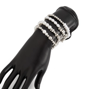 Makroaufnahme von mehrlagigen Perlen- und Silberperlenarmbändern an einer Modellhand