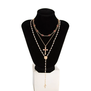 Détail du collier doré à trois rangs avec perles, gemme rouge et pendentif croix