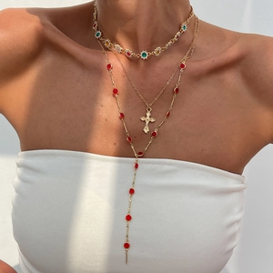 Détail de colliers dorés superposés avec pendentifs en pierres colorées et croix