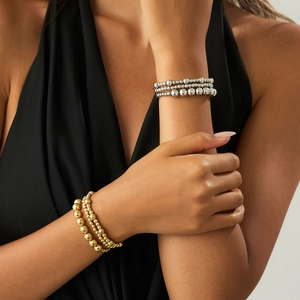 Detail von gestapelten gold- und silberpolierten Metallperlenarmbändern am Handgelenk