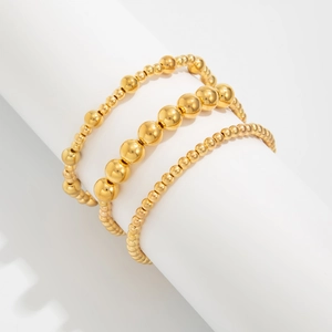 Nahaufnahme eines dreiteiligen goldenen Perlenarmband-Sets auf einem weißen Zylinder