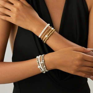 Detail von mehrlagigen Perlenarmbändern mit Kreuzanhängern an einem Model