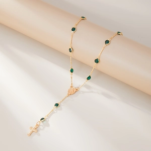 Détail du collier chapelet doré avec perles en cristal vert foncé et pendentif croix
