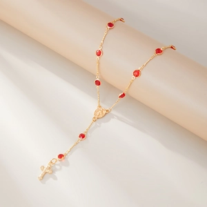 Détail du collier chapelet doré avec cristaux rouges et crucifix sur support beige