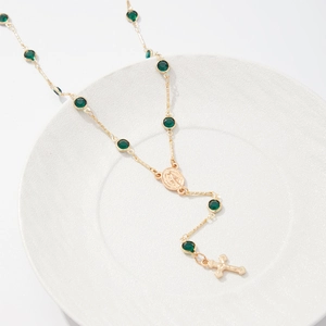Détail du collier en Y doré avec perles de cristal vert, médaille de Marie et une croix