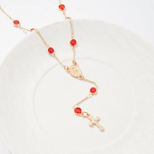 Vue détaillée du collier chapelet doré avec cristaux rouges et pendentif croix