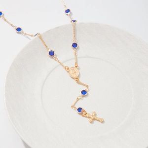 Gros plan du collier en Y doré avec perles bleues et pendentif croix sur plateau blanc