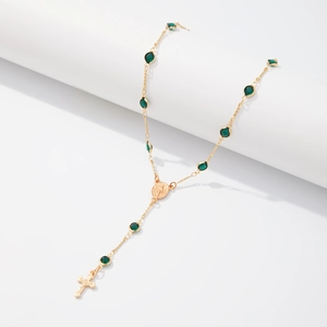 Détail d'un collier rosaire doré avec des perles vertes et un pendentif de crucifix
