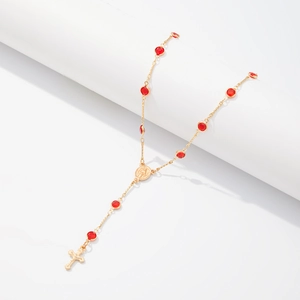 Détail du collier en Y doré avec perles en cristal rouge et pendentif en croix