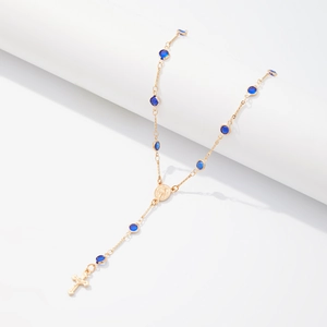 Gros plan des pendentifs croix et médaille dorés avec cristaux bleu foncé sur collier en Y