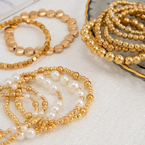 Detailansicht von mehrlagigen Goldperlenarmbändern und weißen Kunstperlen auf Stoff