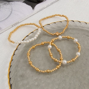 Detail eines vierteiligen Armband-Sets aus Goldperlen und Perlen auf einem Glastablett