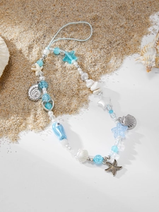 Detailed shot of ocean-themed phone strap with starfish and shell charms on beach sand