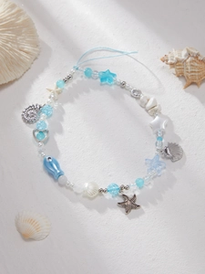 Detail of ocean-themed beaded phone strap with starfish and shell charms on white sand