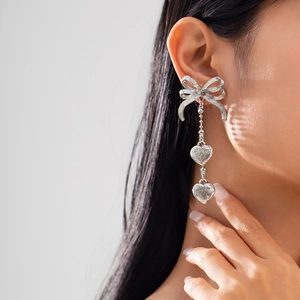 Détail de boucles d'oreilles longues argentées avec nœud et pendentifs en forme de cœur