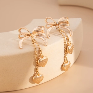 Détail macro de boucles d'oreilles nœud dorées avec zircon, chaînes et cœurs pendus