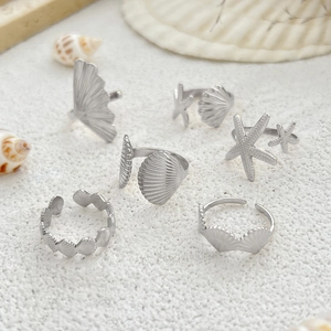 Detailed view of silver sea star and shell adjustable rings on white beach sand
