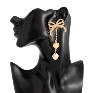 Détail de boucles d'oreilles nœud doré avec cristal et pendentifs cœurs gaufrés