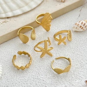 Detail of 6-piece gold starfish and seashell rings set on natural beach background
