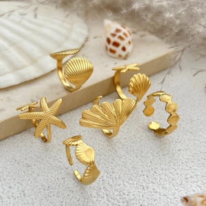 Detailed set of five gold starfish and shell rings on a natural stone and floral backdrop