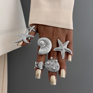 Detailed view of silver sea star and shell rings with white pearl accents on finger