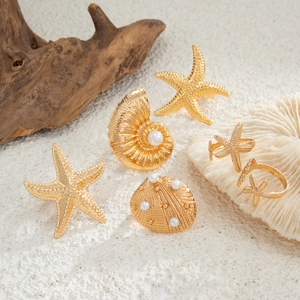 Detailed close-up of gold starfish and shell rings with pearls on white sand