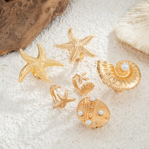 Macro shot of gold starfish and seashell rings with pearls on white sand background