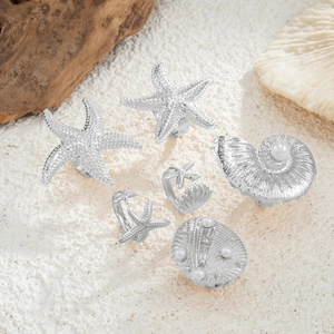 Close-up of silver starfish and shell rings with pearls on a beach sand background