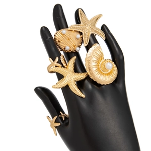 Detailed macro of gold starfish and shell rings with pearls on a black hand model