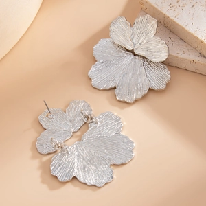 Dettaglio di orecchini a fiore d'argento con petali martellati su sfondo di pietra