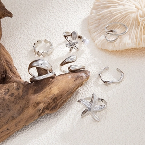 Silver starfish and shell rings on white coral and driftwood in a coastal scene