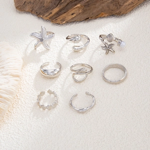 Detailed view of 8-piece silver starfish and shell rings on a sandy background