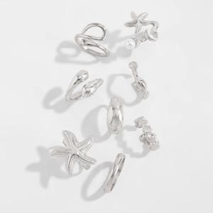 Detailed view of a 7-piece silver starfish and shell themed rings set on white background