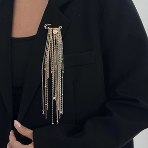 Detail einer mehrlagigen Herz-Quasten-Brosche mit Gold- und Silberketten am schwarzen Blazer
