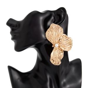 Dettaglio di orecchino a fiore dorato con petali metallici testurizzati e perla