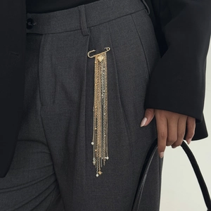 Detail einer goldenen Herz-Quasten-Brosche an einer Anzughose für einen Look