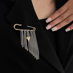 Detail einer Metallnadel-Brosche mit Herzanhänger und silbernen Fransen auf schwarzem Blazer