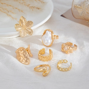 Gedetailleerde set van 6 gouden ringen met parels en bloemmotieven op getextureerde doek