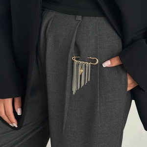 Dettaglio spilla da balia con nappine a catena argento e cuore dorato sui pantaloni