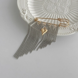 Dettaglio di spilla a balia dorata con nappe a catena e pendente a forma di cuore