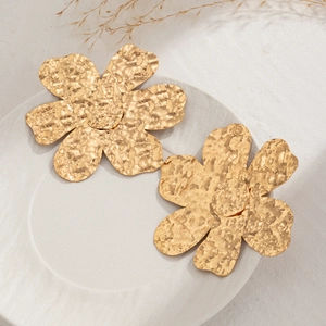 Dettaglio di orecchini a fiore in oro martellato su un vassoio grigio decorativo